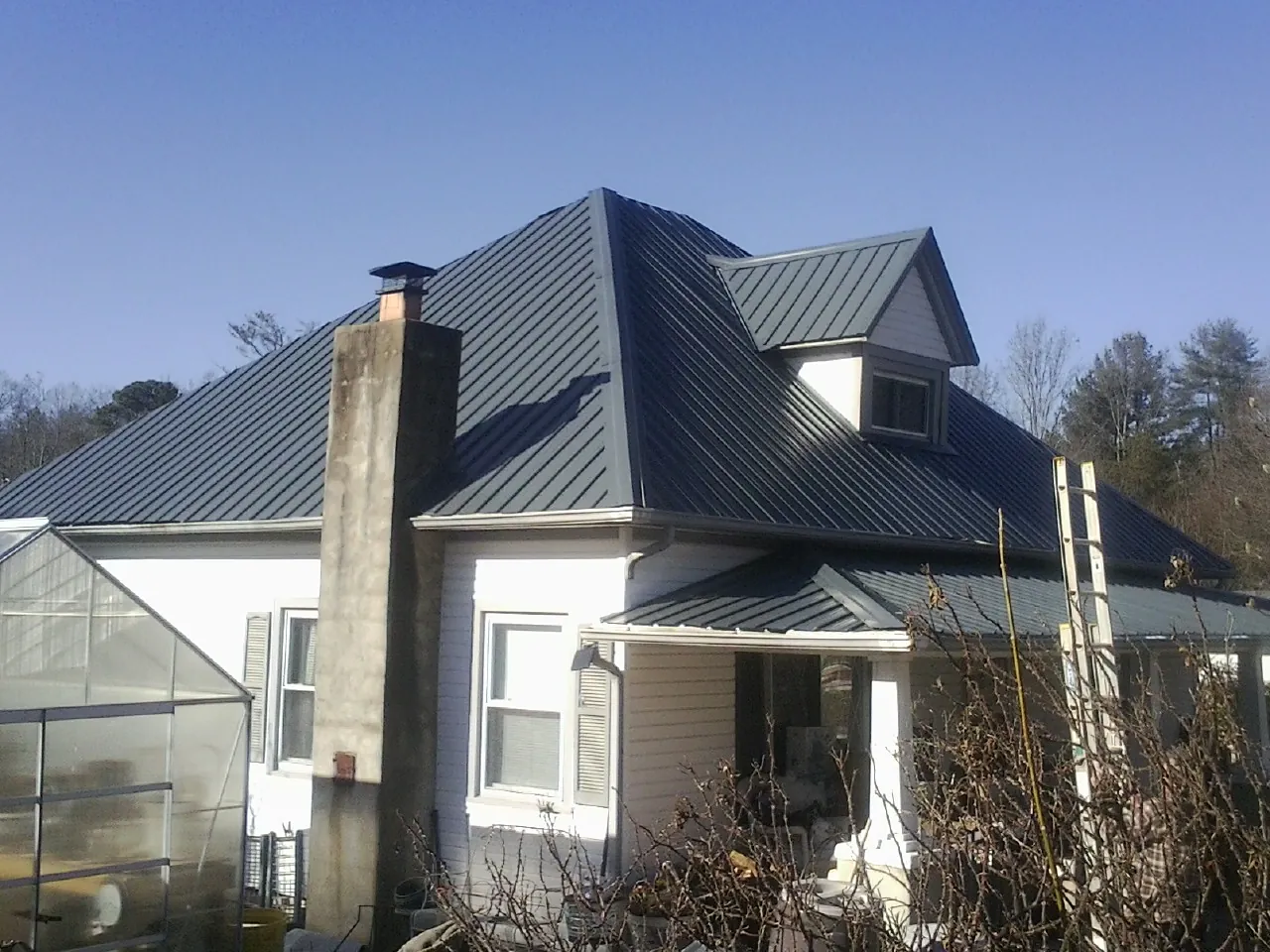 Dark blue standing seam metal roof on a white farmhouse with dormer — Slate & Tile Roof Repair by Roofing Brothers in Bellaire