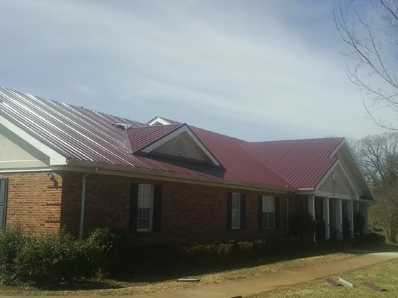 Red metal roof with gabled entries on a long brick building, from a Hail Damage Roof Repair job in Bellaire