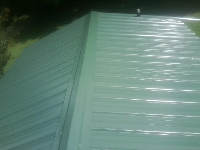 New green metal panels meeting at the ridge of a roof — Flat Roof Repair work by our crew in Bellaire